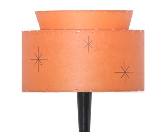 May include: A two-tiered orange lampshade with a black base. The lampshade has a starburst pattern.