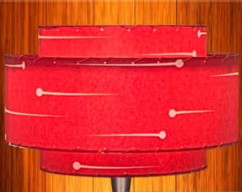 May include: A red, tiered lampshade with white accents. The shade has a retro design with a cylindrical shape and a smaller top tier. White lines and dots decorate the red surface. The lamp is a decorative lighting fixture.