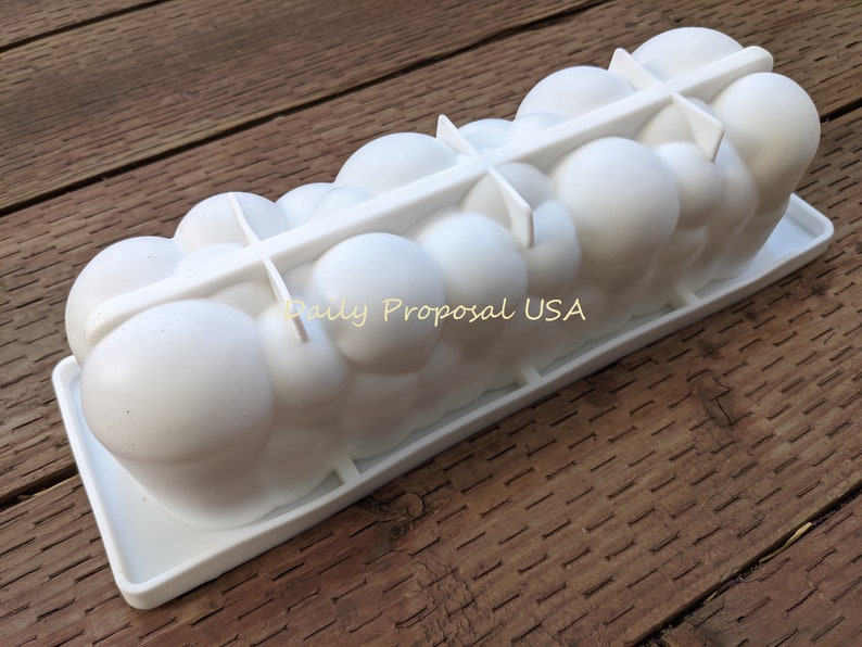 May include: A white silicone mould in the shape of clouds, suitable for baking or crafts. It features a rectangular base and a series of rounded, bubble-like shapes. The text "Daily Proposal USA" is visible.