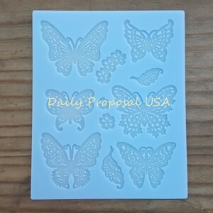 May include: A light blue silicone mold featuring various butterfly and floral designs. The mold includes butterflies of different sizes and styles, along with small flower and leaf shapes. The text "Daily Proposal USA" is printed on the mold.