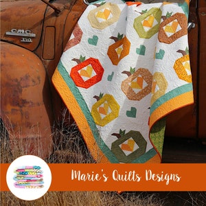 May include: A quilt with a harvest theme featuring a patchwork of pumpkins in various shades of orange, yellow, and green. The quilt is draped over the side of a rusty truck. The text "Harvest Time" is displayed at the top of the image. The text "Marie's Quilts Designs" is displayed at the bottom of the image.