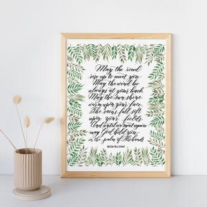May include: A framed print with an Irish blessing in elegant calligraphy. The text is surrounded by a border of green watercolor leaves. The frame is made of light-colored wood. A small beige vase with dried flowers is on the left.