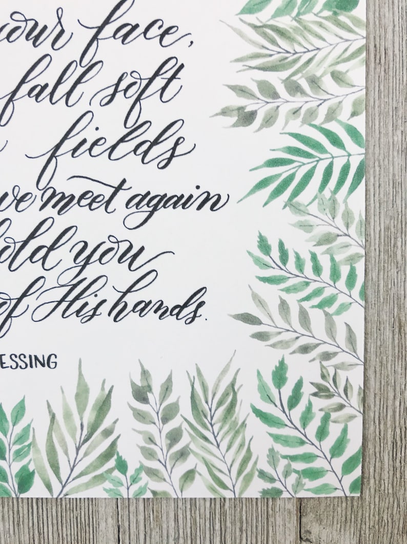 May include: A white paper print with elegant black calligraphy text and watercolor botanical illustrations. The text reads "our face, fall soft fields, we meet again, hold you, of His hands, BLESSING". Green leaves and branches frame the edges.