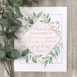 May include: A watercolour print with a gold frame and pink flowers. The print features a quote that reads "Blessed assurance Jesus is mine! Oh what a foretaste of glory divine!"