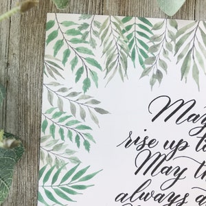 May include: A white card with a watercolor design of green leaves and branches. The card has elegant black calligraphy text that reads "May the..." and continues with additional script. The leaves frame the top and left side of the card.