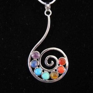 May include: Silver pendant necklace with a spiral design, incorporating seven gemstones in a rainbow spectrum. The necklace has a silver chain and is set against a black backdrop. The gemstones are in a rainbow spectrum.