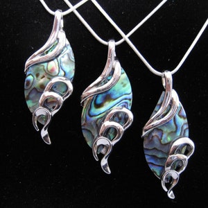 May include: Three silver pendant necklaces with iridescent abalone shell teardrop-shaped pendants. Each pendant has a silver swirl design on the side. The necklaces are displayed against a black background.