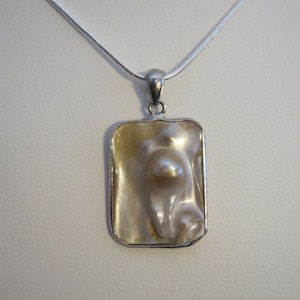 May include: A silver necklace with a rectangular pendant. The pendant features a large, irregularly shaped, off-white pearl framed by a silver border. The pearl has a lustrous, iridescent quality.