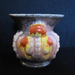 Op de afbeelding: Een vintage keramische vaas met een brede, uitlopende rand en een bolvormig lichaam. De vaas heeft een roze, gele en oranje bloemenmotief met een donkerbruine rand en voet. De vaas heeft een uniek, getextureerd oppervlak.