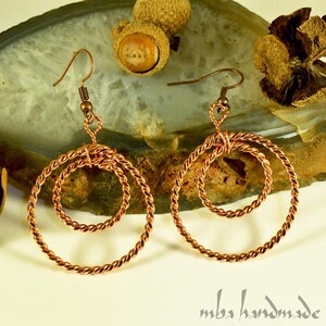 May include: A pair of copper wire earrings with a double circle design. The earrings are handmade and have a rustic, earthy look.