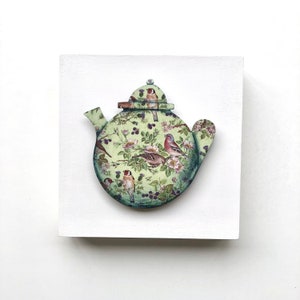 May include: A green teapot with a floral pattern featuring birds and berries. The teapot is made of wood and has a 3D effect.