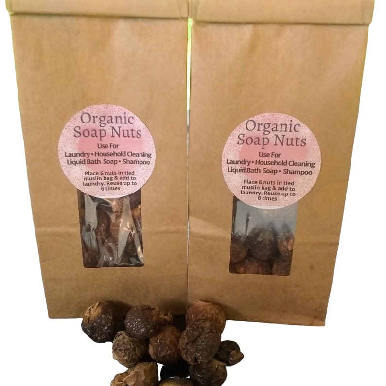 May include: Two brown paper bags with a clear window showing brown soap nuts inside. The bags have a white label with the text "Organic Soap Nuts" and instructions for use. The text on the label reads: "Use For Laundry Household Cleaning Liquid Bath Soap Shampoo Place 6 nuts in tied muslin bag & add to laundry. Reuse up to 6 times."