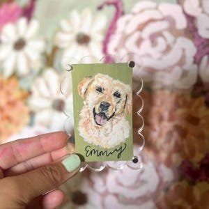 May include: A rectangular acrylic plaque with a scalloped edge featuring a painted portrait of a golden dog on a sage green background. The name Emmy is written in black cursive script at the bottom of the portrait. The plaque is clear acrylic.