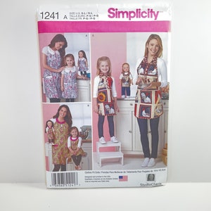 May include: Simplicity sewing pattern number 1241 for making clothes for 18-inch dolls. The pattern includes four different outfits: a red and white gingham dress, a floral print dress, a sunflower print dress, and a rooster print dress. The pattern is designed and printed in the USA.