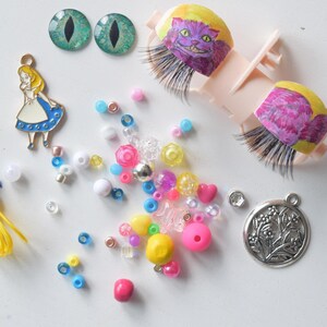 Pode incluir: Uma coleção de materiais de artesanato, incluindo um berloque de metal da Alice no País das Maravilhas, dois cabochões verdes com olhos de gato, cílios postiços com um design do Gato Cheshire e várias contas coloridas. Um cordão amarelo com uma fita azul também está incluído.