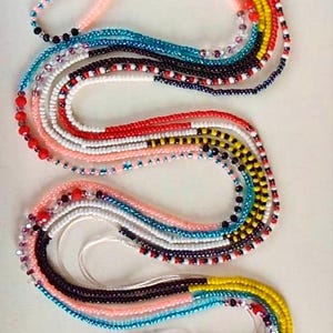 May include: A colorful beaded necklace with multiple strands of beads in various colors, including red, white, blue, yellow, and black. The beads are arranged in a pattern, creating a visually appealing design.