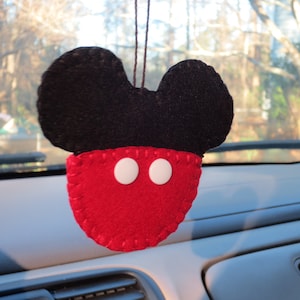 May include: A red felt Mickey Mouse car air freshener with black ears and white eyes. The air freshener is hanging from a string.