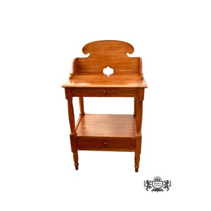 May include: A wooden side table with two shelves and a drawer. The table has a carved top with a cutout design. The table is made of light wood and has a natural finish.