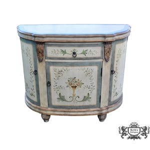 May include: A semi-circular wooden cabinet featuring a light blue and cream finish with hand-painted floral motifs. The piece includes one central drawer and a cabinet door, both adorned with dark metal ring pulls and fluted column details.