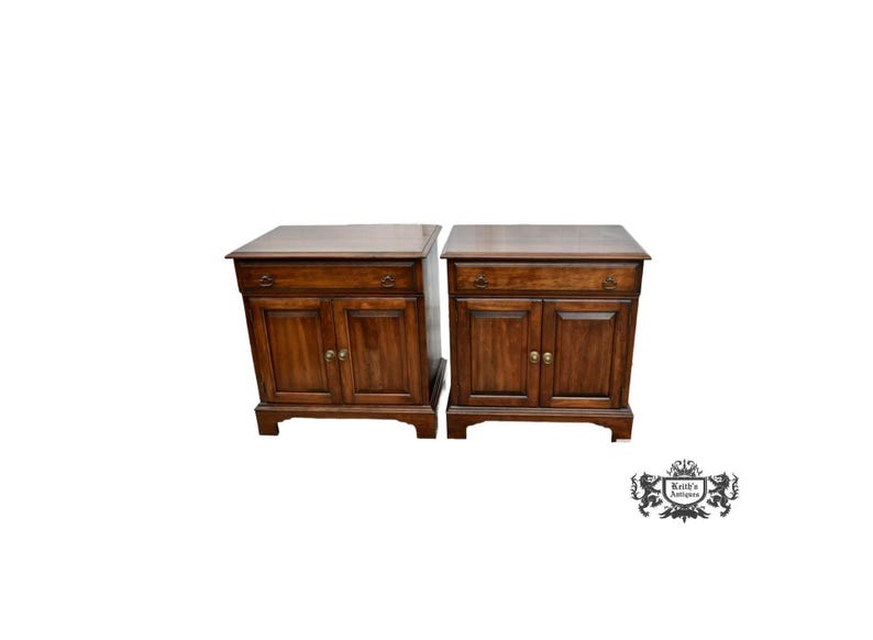 May include: Two matching wooden nightstands with a dark brown finish. Each nightstand has a drawer, two cabinet doors, and brass-colored hardware. The nightstands are on a white background.