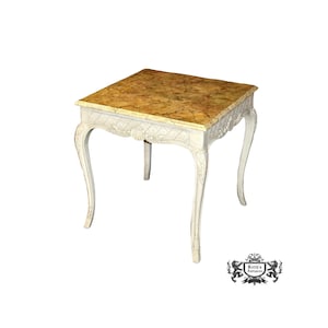 May include: White painted end table with a carved design on the apron and legs. The table top is made of a light brown marble with a marbled pattern.