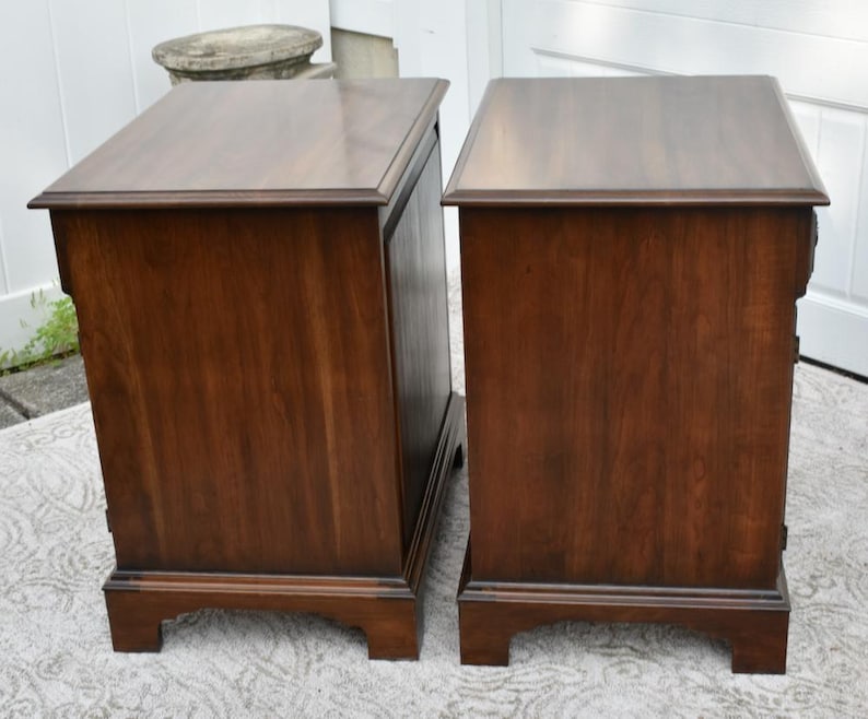 May include: Two matching wooden nightstands with a rich, dark brown finish. Each nightstand features a rectangular top, a single drawer, and a decorative base. The nightstands are placed side by side, showcasing their similar design and construction.