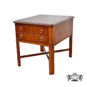 May include: A wooden side table with two drawers and brass ring pulls. The table has a rectangular top and is supported by four legs. The wood has a warm, reddish-brown tone. The table is a classic piece of furniture.