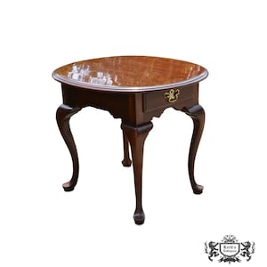 May include: A dark brown, antique side table with a round top and a single drawer. The table has curved legs and a decorative brass drawer pull. The table is approximately 24 inches in diameter and 26 inches tall.
