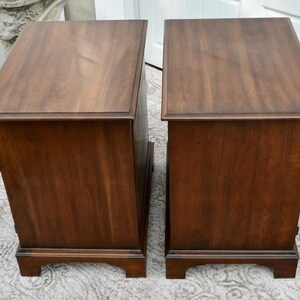 May include: Two matching wooden nightstands with a rich, dark brown finish. Each nightstand has a rectangular top, a single drawer, and a decorative base. The wood grain is visible, adding to the classic aesthetic.