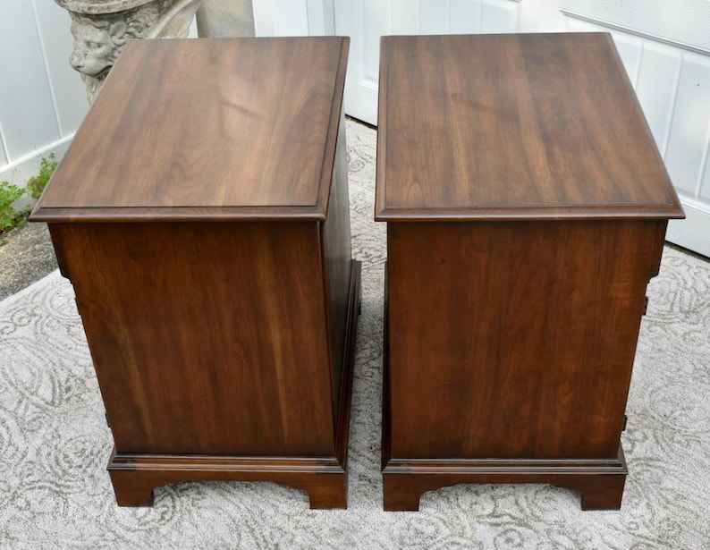 May include: Two matching wooden nightstands with a rich, dark brown finish. Each nightstand has a rectangular top, a single drawer, and a decorative base. The wood grain is visible, adding to the classic aesthetic.
