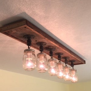 Pu&ograve; includere: Un lampadario rustico per soffitto in legno riciclato con sei luci in barattolo di muratore appese ad esso.
