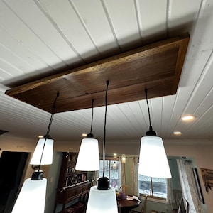 May include: A wooden ceiling fixture with five white glass pendant lights hanging from black cords.