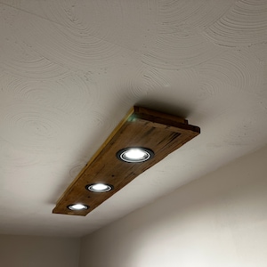 May include: A wooden ceiling light fixture with four recessed lights. The fixture is made of reclaimed wood and has a rustic look.