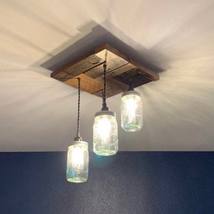 May include: A rustic ceiling light fixture made from reclaimed wood with three mason jar pendant lights. The jars are clear glass with a light bulb inside each one.