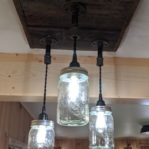 May include: A rustic ceiling light fixture made from reclaimed wood with three mason jar lights hanging from black cords.