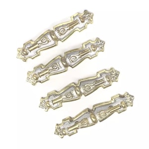 May include: Four ornate gold and silver metal drawer pulls with a decorative design. The pulls are arranged in a staggered pattern.