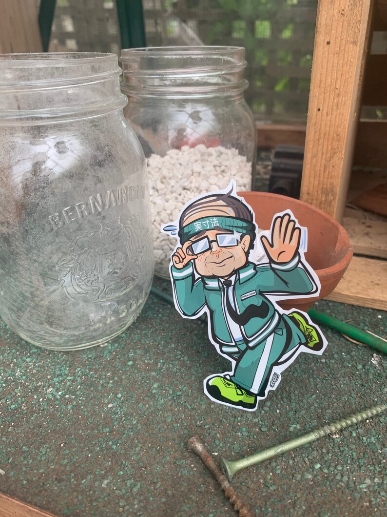 May include: A cartoon sticker of a man wearing a green headband with the text "実力" in white, green glasses, a green jacket, and white pants. He is running with his right arm raised and his left hand holding a fist. The sticker is on a brown surface with a green background.
