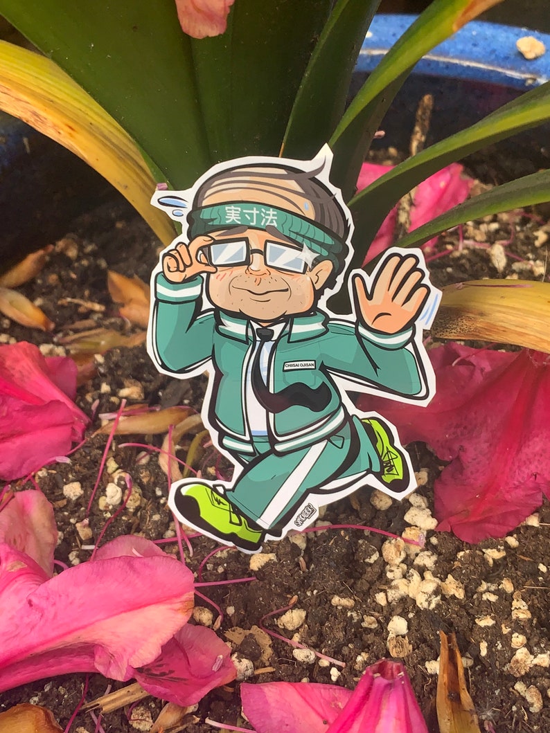 May include: A cartoon sticker of a person wearing a green jacket, white pants, and a headband that says "実力" in Japanese. The person is wearing glasses and has a mustache. The sticker is placed on a bed of pink flower petals.