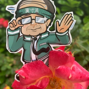 May include: A cartoon sticker of a person wearing a green jacket, glasses, and a headband that says "実寸法". The sticker is placed on a pink rose.