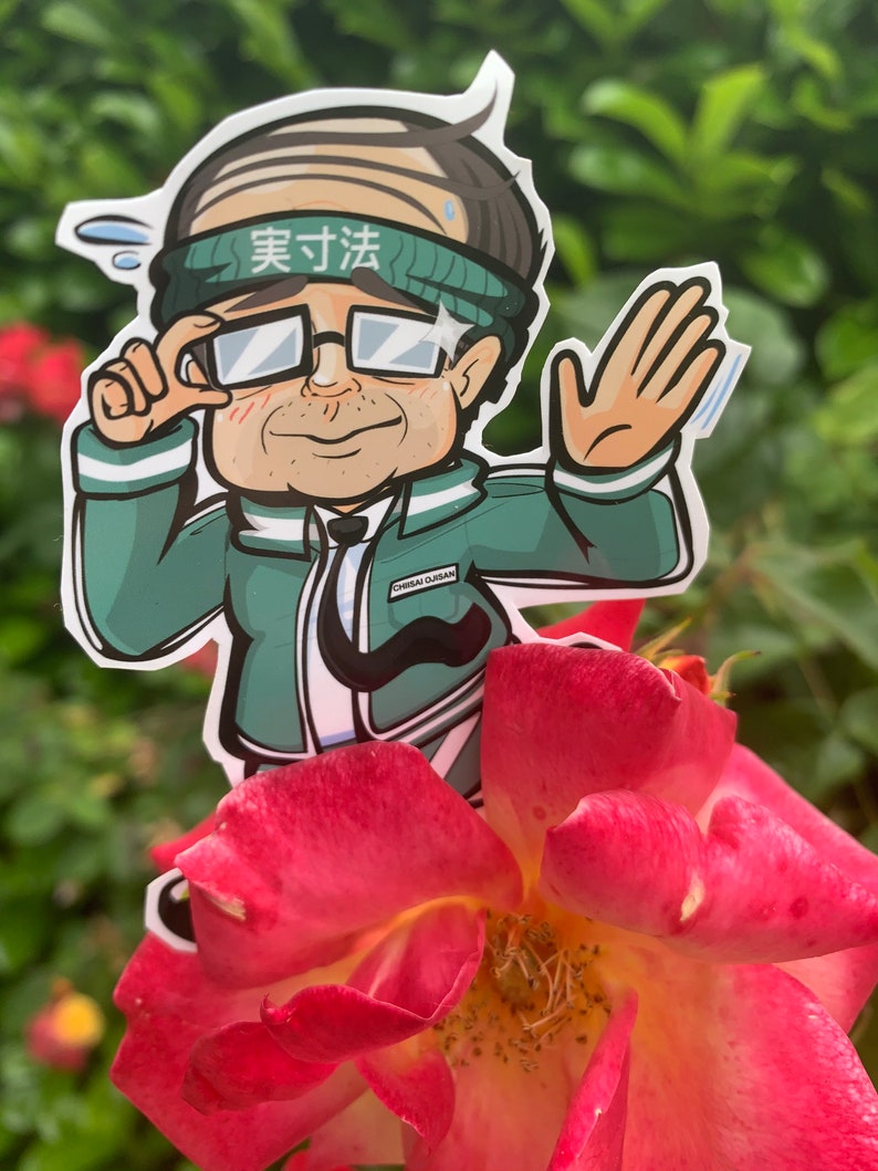May include: A cartoon sticker of a person wearing a green jacket, glasses, and a headband that says "実寸法". The sticker is placed on a pink rose.