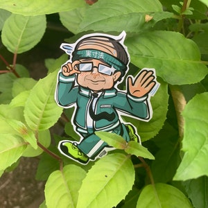 May include: A green and white cartoon sticker of a person wearing a headband with the text "実力派" in Japanese. The person is wearing glasses and a green jacket with a white stripe. The person is holding their hand up in a wave.