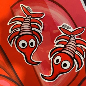 May include: Two red and white cartoon stickers of a creature with large eyes and a segmented body. The stickers are labelled "Arthro-Embyro" and "Swimeksy".