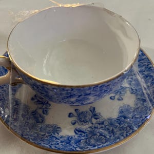 May include: A blue and white teacup and saucer set with a floral pattern and gold trim.