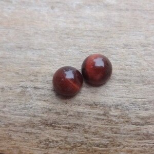 May include: Two round red tiger's eye cabochons on a wooden surface.