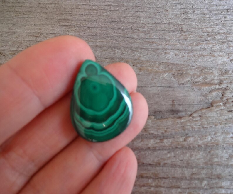 K&ouml;nnte beinhalten: Ein tropfenf&ouml;rmiger gr&uuml;ner Malachit-Edelstein mit konzentrischen Ringen aus dunklerem Gr&uuml;n.