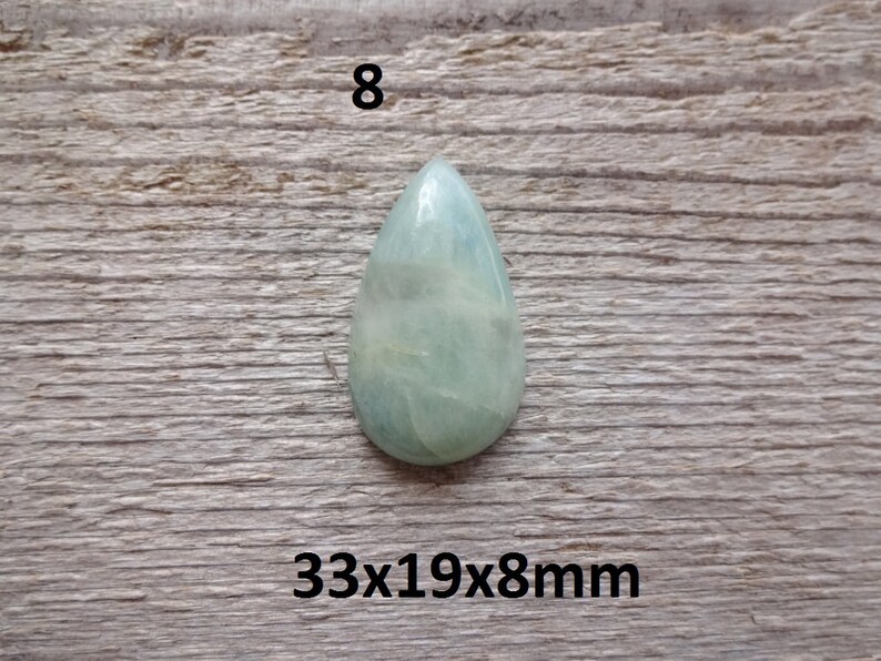 K&ouml;nnte beinhalten: Ein hellgr&uuml;ner, tropfenf&ouml;rmiger Edelstein mit wei&szlig;en Adern. Der Edelstein misst 33x19x8mm.