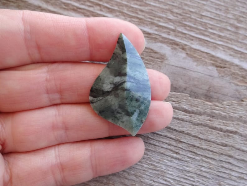 Puede incluir: Un cabuj&oacute;n de piedra verde y gris con una forma &uacute;nica en forma de hoja. La piedra tiene un patr&oacute;n de remolino de verde oscuro y claro.