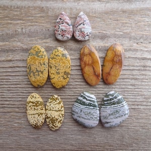 May include: Assortment of eight polished oval and teardrop shaped stones with various patterns in shades of brown, yellow, white, and gray.