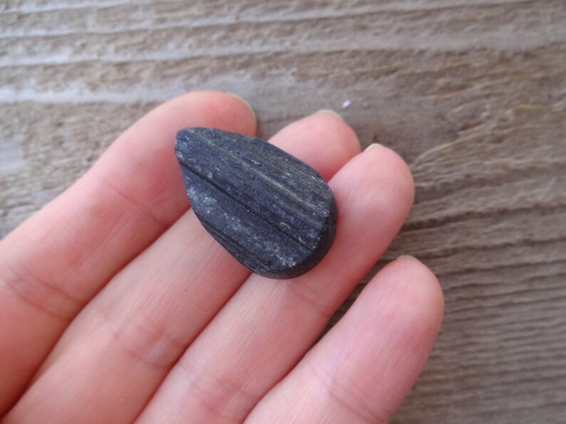 May include: A black teardrop-shaped stone with a striated surface.