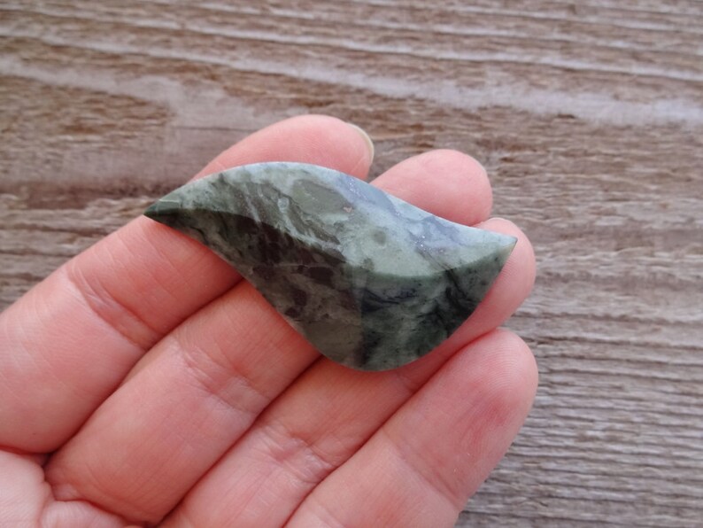 Puede incluir: Una piedra verde y negra con una forma org&aacute;nica &uacute;nica. La piedra es lisa y pulida, con un patr&oacute;n de remolino de verde y negro.